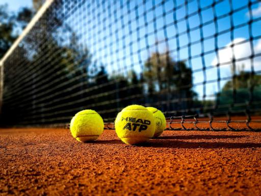 Tennisplatz im Freien mit Netz und drei Tennisbällen im Vordergrund und Bäumen im Hintergrund